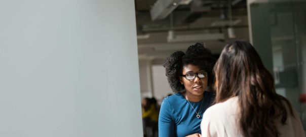 Two women engaged in a discussion in a modern office environment, highlighting communication and interaction.