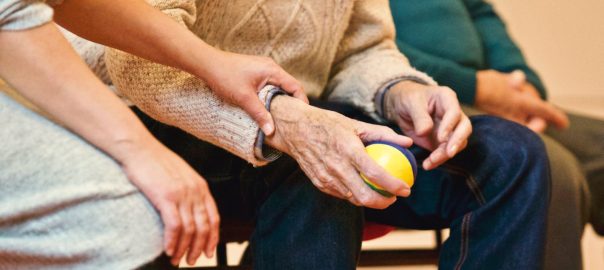 An elderly person receives support from a caregiver, holding hands indoors, showcasing compassion.