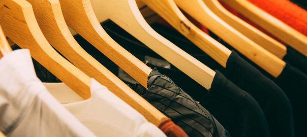 A close-up view of a row of clothes on wooden hangers, showcasing various fabrics and colors in a wardrobe setting.